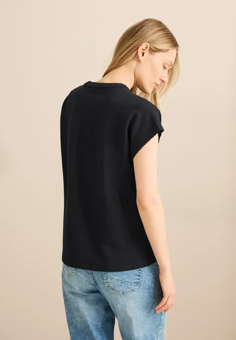Frau mit blondem Haar, schwarzem Shirt und Jeans, von hinten fotografiert.